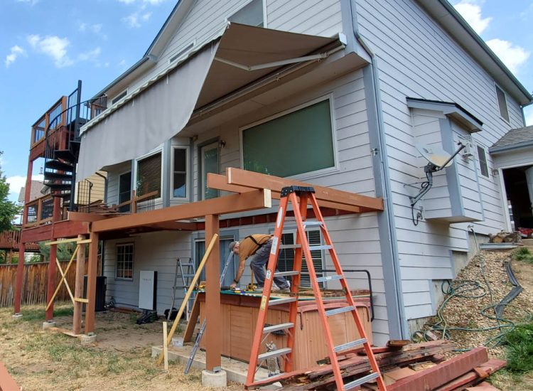 A mid-construction view of a multi-tier deck being built on the back of a house, featuring various construction materials and tools in use.