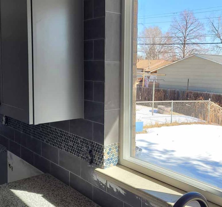 A modern kitchen featuring dark tiles, a decorative border, and a view out to a snowy backyard through a large window, offering natural light and a serene outdoor view.