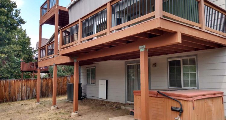 A spacious wooden deck featuring a hot tub and multiple levels, set against a fenced backyard, illustrating a family-friendly outdoor living space.