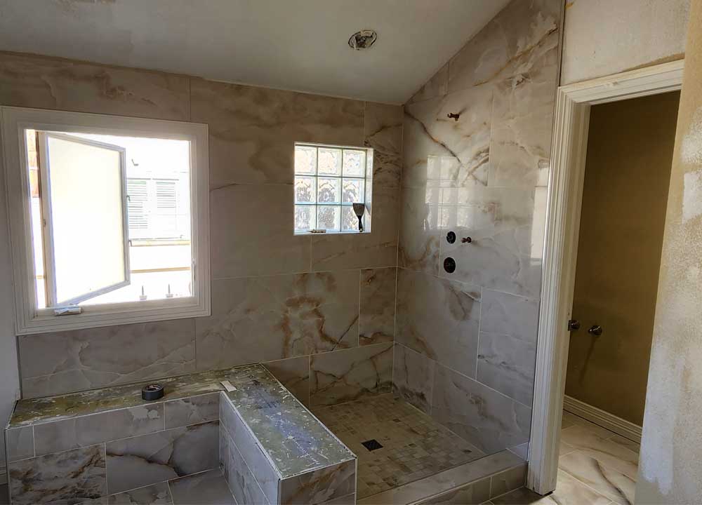 A spacious bathroom showing extensive use of marble tiles, with a large shower area featuring a built-in bench.