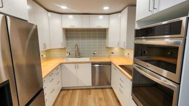 A modern U-shaped kitchen featuring white cabinetry, butcher block countertops, stainless steel appliances, and a tiled backsplash.